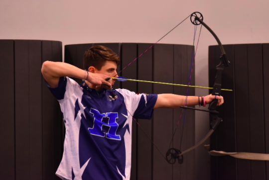 Senior Ethan Stuart, Archery Team co-captain, draws his bow back and aims towards the target. 