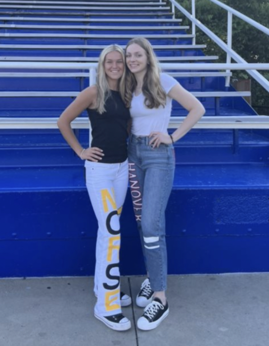 Seniors CC Shick and Meg Gessner pose for a picture with their future colleges painted on jeans after the sleepover.