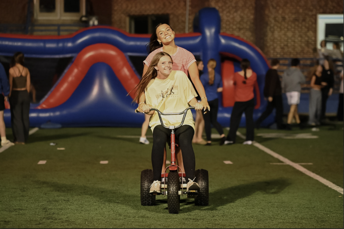 Payton Brown (12) and Kaitlyn Dixon (12) ride a tricycle together.  "I really liked the outside activities at prom to dawn because I got to be with all my friends," Brown (12) said.